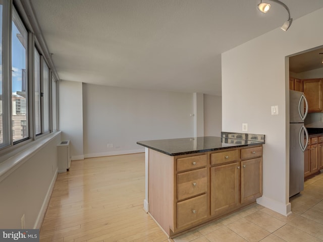 kitchen with radiator, brown cabinetry, freestanding refrigerator, dark stone countertops, and a peninsula