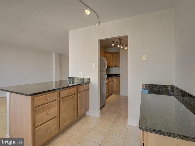 kitchen with light tile patterned flooring, a peninsula, freestanding refrigerator, dark stone countertops, and track lighting