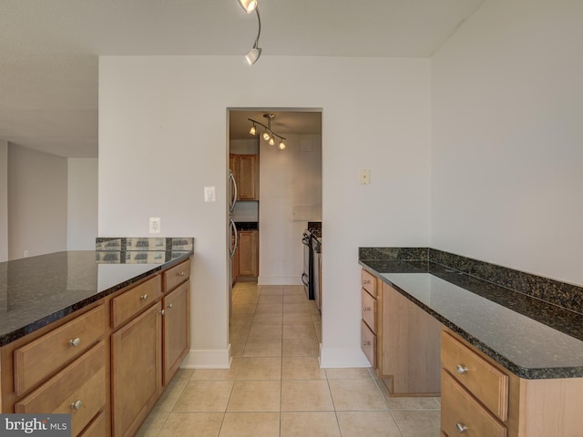 kitchen featuring light tile patterned floors, dark stone counters, brown cabinetry, a peninsula, and fridge