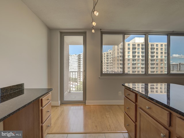 interior space with light wood-type flooring, dark stone countertops, and a textured ceiling