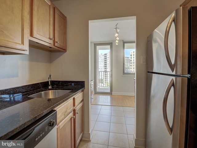 kitchen with light tile patterned floors, stainless steel appliances, a sink, baseboards, and dark stone counters