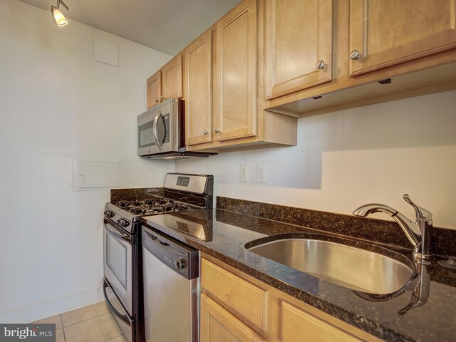 kitchen with light tile patterned floors, stainless steel appliances, a sink, dark stone countertops, and baseboards