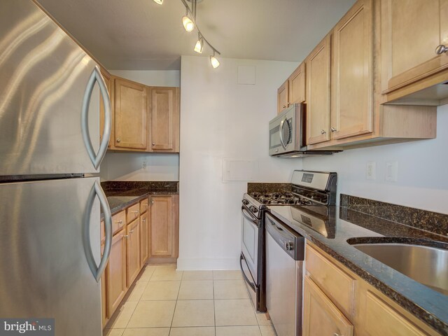 kitchen featuring stainless steel appliances, track lighting, light brown cabinets, dark stone counters, and light tile patterned flooring