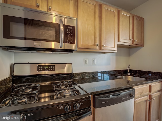 kitchen with dark stone countertops, appliances with stainless steel finishes, and a sink