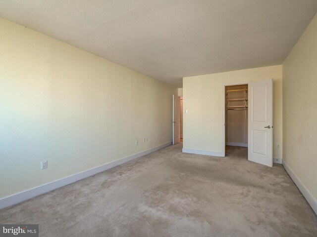 unfurnished bedroom featuring light carpet, a textured ceiling, a spacious closet, and a closet