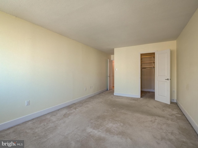 unfurnished bedroom featuring a closet, light colored carpet, a spacious closet, and baseboards