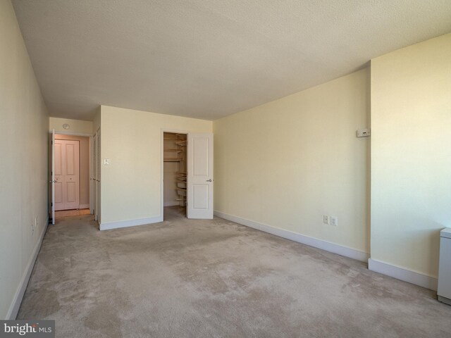 unfurnished bedroom featuring a closet, a spacious closet, light carpet, and a textured ceiling