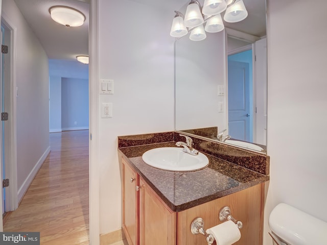 bathroom featuring toilet, baseboards, wood finished floors, and vanity