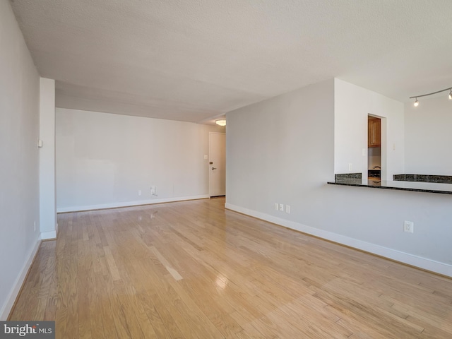 empty room with a textured ceiling, light wood-style flooring, and baseboards