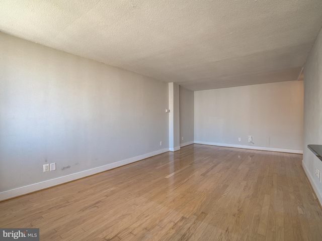 unfurnished living room with light wood-type flooring, baseboards, and a textured ceiling