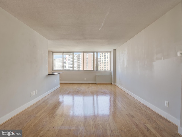 empty room with a textured ceiling, baseboards, and wood finished floors