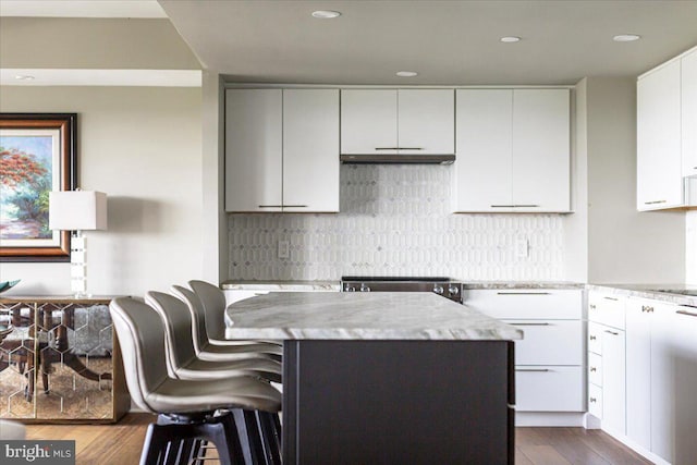 kitchen featuring white cabinetry, a center island, light stone countertops, dark hardwood / wood-style floors, and a breakfast bar