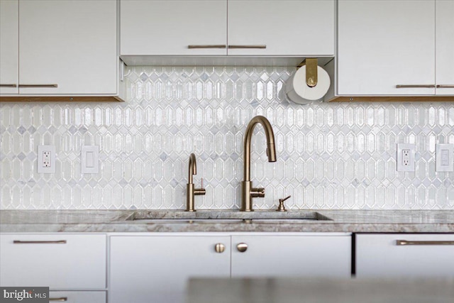 details featuring backsplash, light stone countertops, and sink