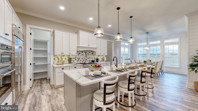 kitchen featuring white cabinets, light hardwood / wood-style floors, pendant lighting, decorative backsplash, and a center island with sink