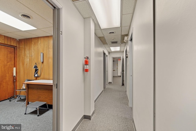 corridor featuring wooden walls, a drop ceiling, visible vents, and light colored carpet