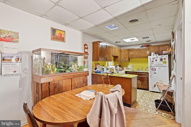 kitchen featuring white fridge, light hardwood / wood-style flooring, kitchen peninsula, sink, and a paneled ceiling