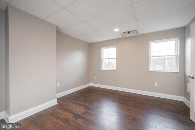 empty room featuring dark wood-style flooring, visible vents, a drop ceiling, and baseboards