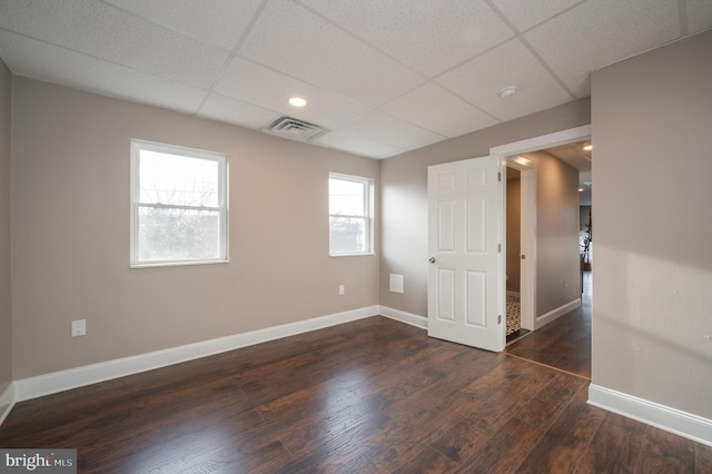 spare room featuring a paneled ceiling, dark wood-style flooring, visible vents, and baseboards