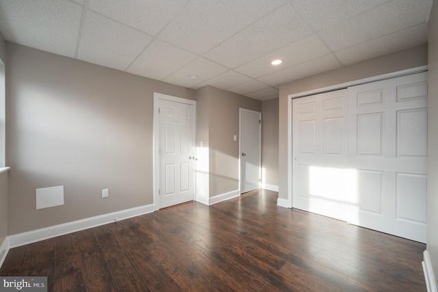 unfurnished bedroom featuring baseboards, a drop ceiling, and dark wood-style flooring