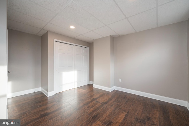 unfurnished bedroom with a paneled ceiling, dark hardwood / wood-style flooring, and a closet