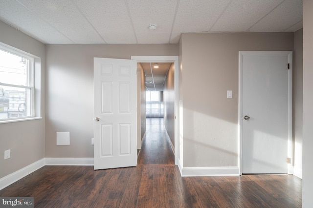 unfurnished room featuring dark wood-style flooring, a paneled ceiling, and baseboards