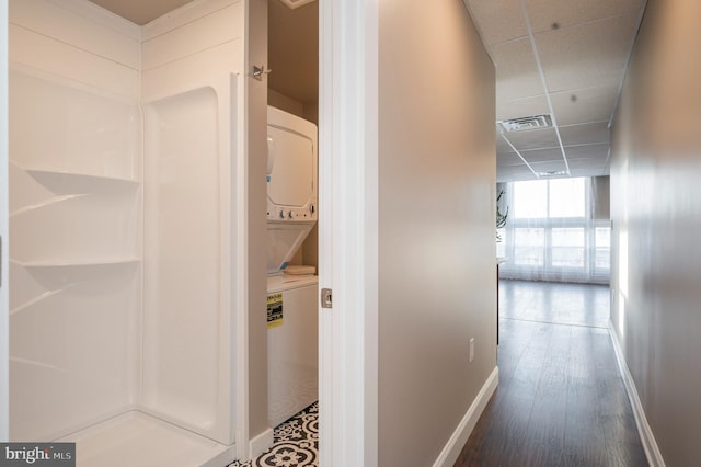 hall with stacked washer and clothes dryer, visible vents, wood finished floors, a drop ceiling, and baseboards