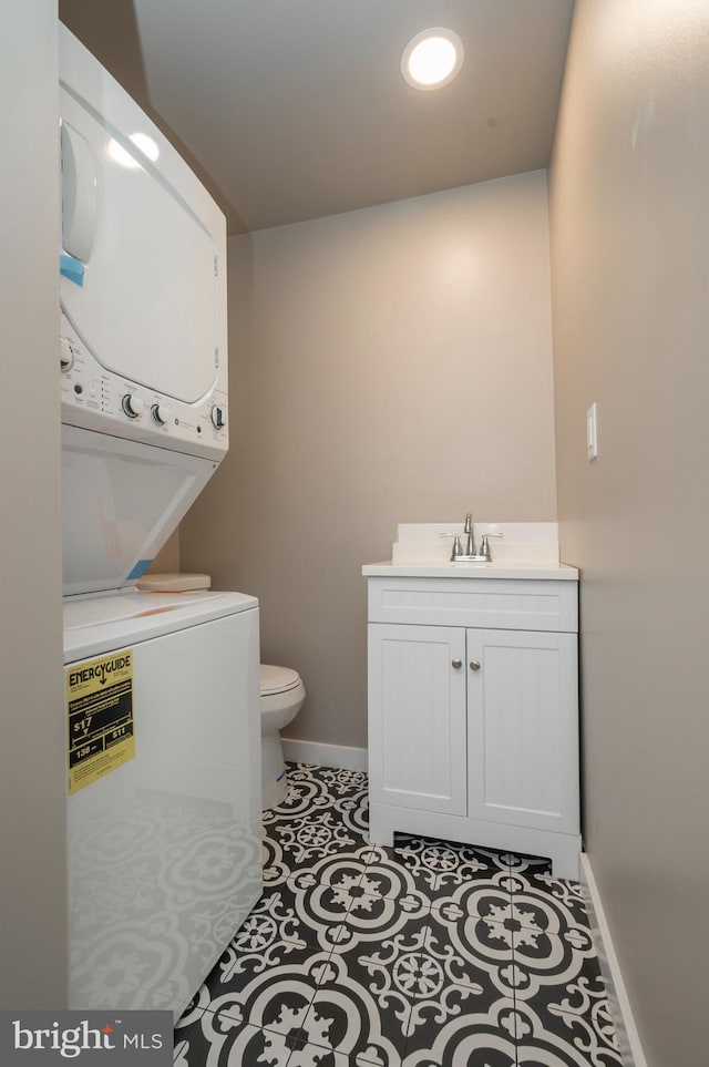 half bathroom with stacked washer and dryer, baseboards, toilet, tile patterned flooring, and vanity