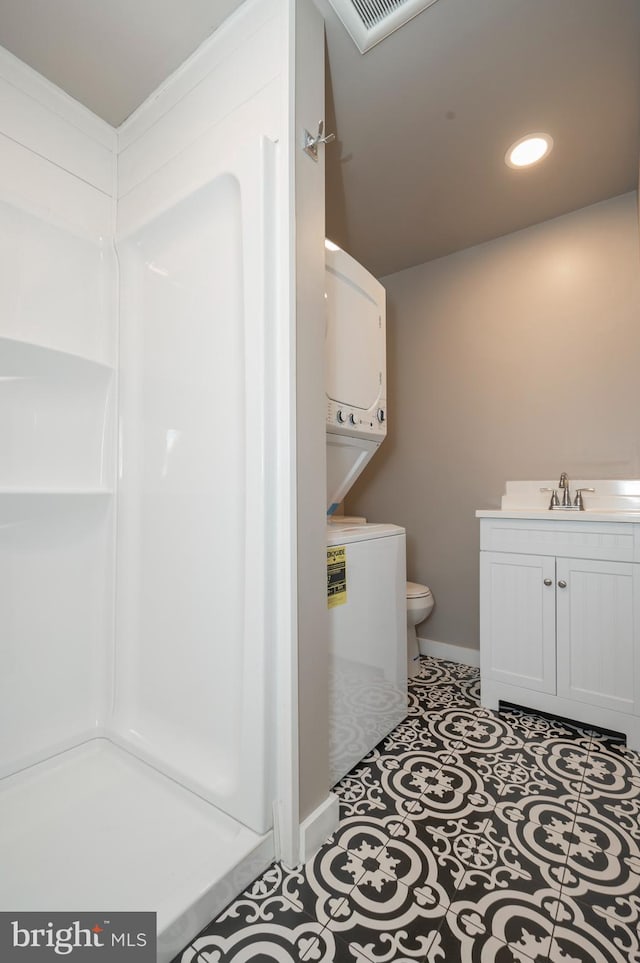 bathroom featuring toilet, tile patterned flooring, vanity, a shower, and stacked washer and clothes dryer