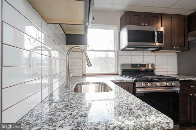 kitchen with stainless steel appliances, sink, light stone countertops, and backsplash