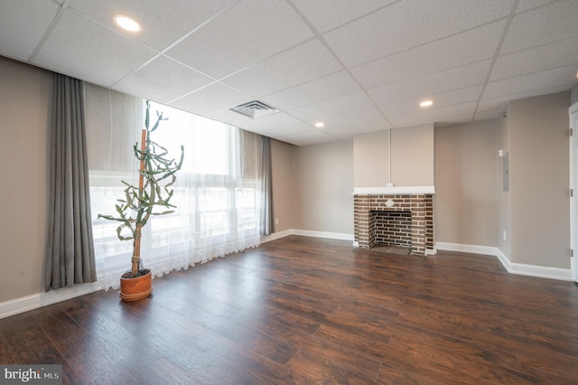 unfurnished living room with a brick fireplace, dark hardwood / wood-style flooring, and a drop ceiling