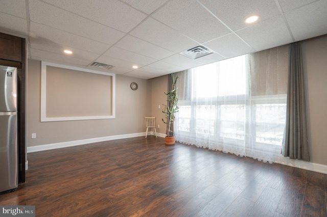 empty room with a drop ceiling, dark wood finished floors, visible vents, and baseboards