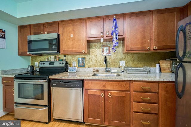 kitchen with light wood-type flooring, sink, tasteful backsplash, appliances with stainless steel finishes, and light stone countertops