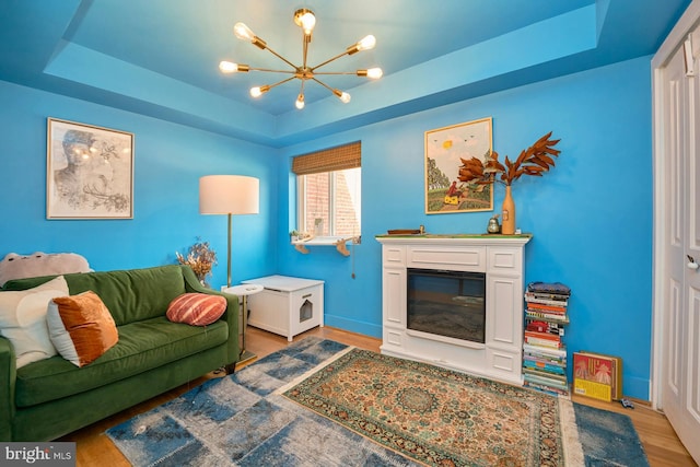 living room with an inviting chandelier, a raised ceiling, and hardwood / wood-style floors