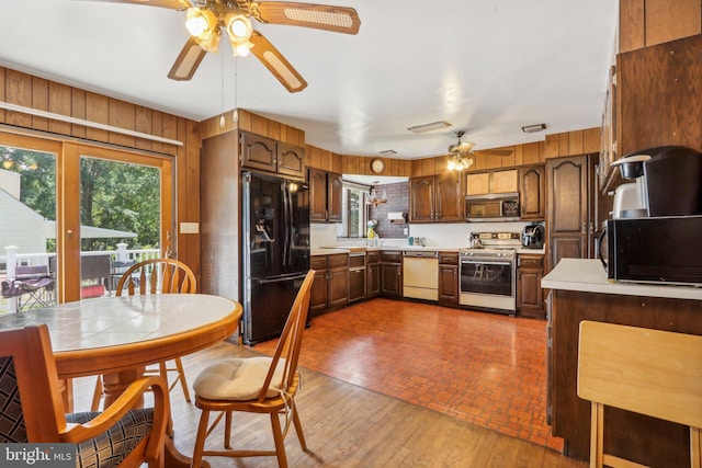 kitchen featuring wooden walls, black appliances, wood-type flooring, sink, and ceiling fan