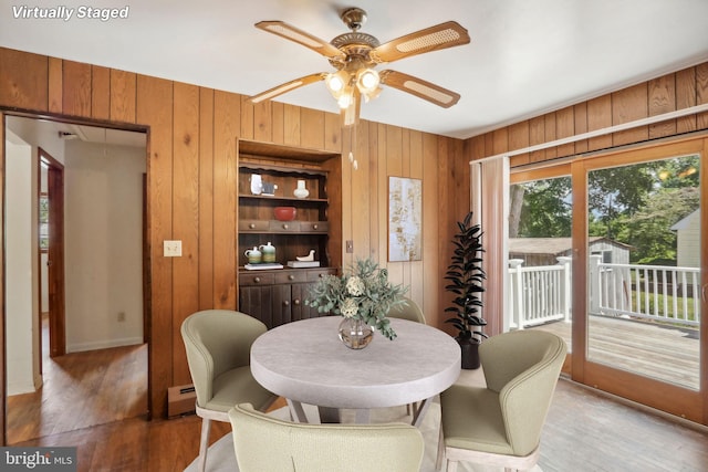 dining room featuring a baseboard heating unit, ceiling fan, wood walls, and wood-type flooring