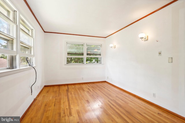 spare room featuring light wood-type flooring, ornamental molding, and a healthy amount of sunlight