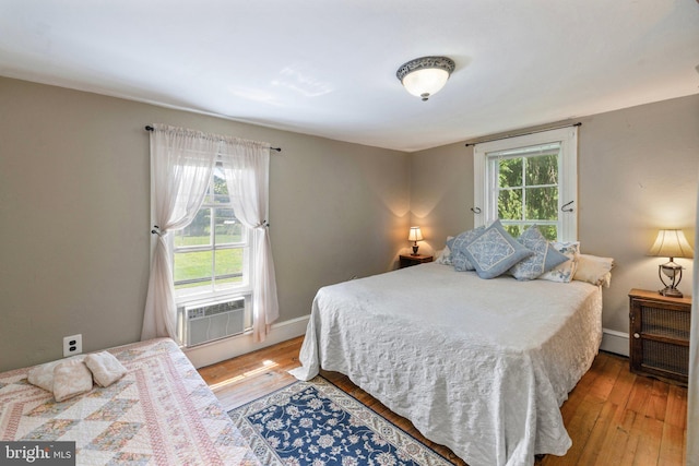 bedroom with cooling unit, multiple windows, baseboards, and wood finished floors