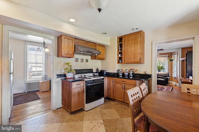 kitchen featuring ventilation hood, light tile patterned floors, white gas range, a chandelier, and radiator heating unit