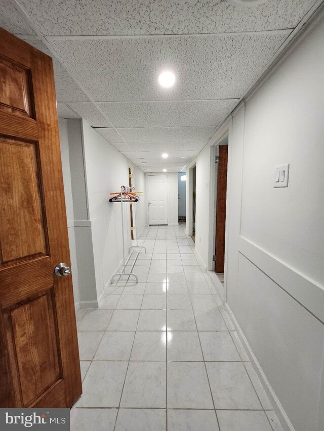 hall featuring light tile patterned floors, a drop ceiling, and baseboards