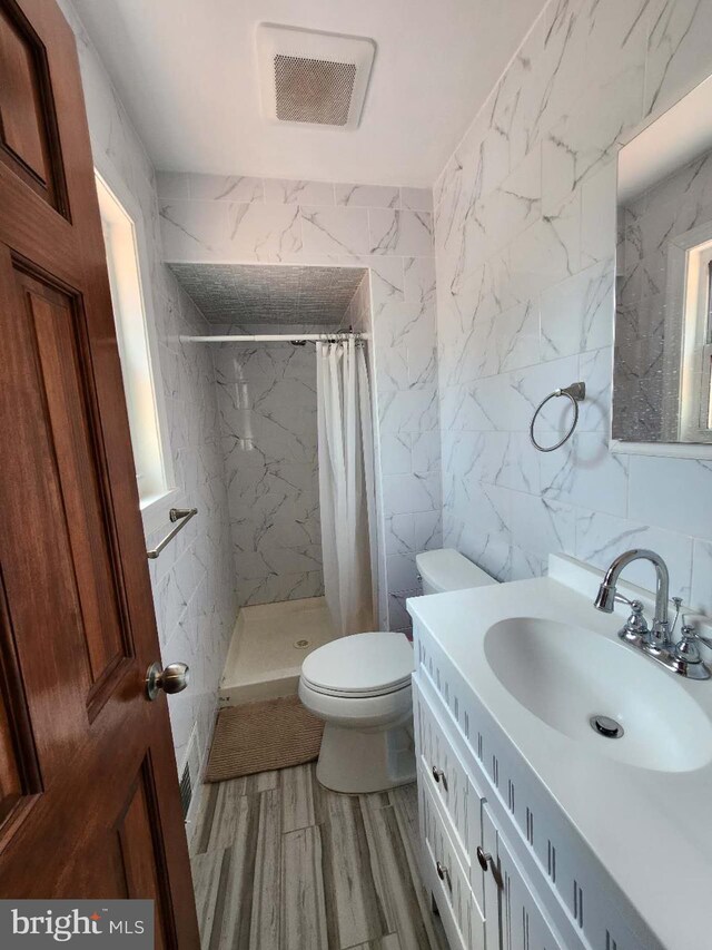 bathroom featuring toilet, vanity, visible vents, tile walls, and a stall shower