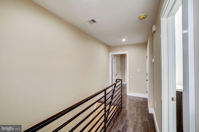 hall with dark wood finished floors, an upstairs landing, visible vents, and baseboards