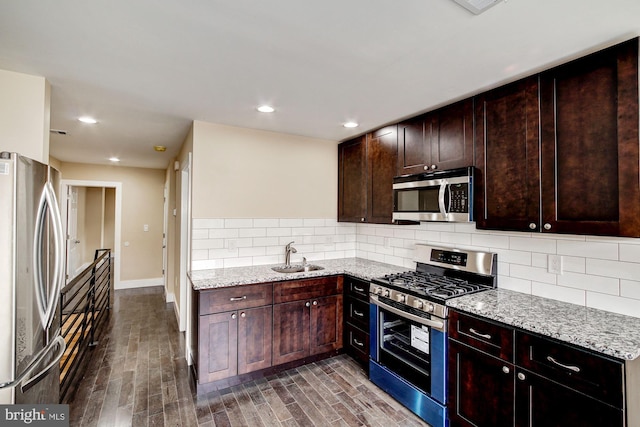 kitchen featuring light stone counters, stainless steel appliances, decorative backsplash, dark wood-type flooring, and a sink