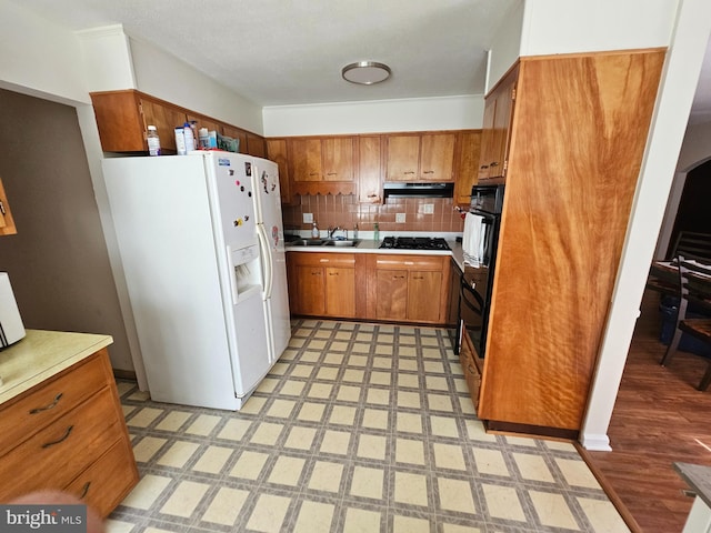 kitchen featuring backsplash, light tile patterned floors, white refrigerator with ice dispenser, black gas stovetop, and sink