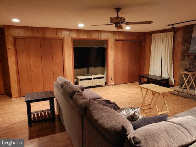 living room with ceiling fan, wood-type flooring, and wooden walls