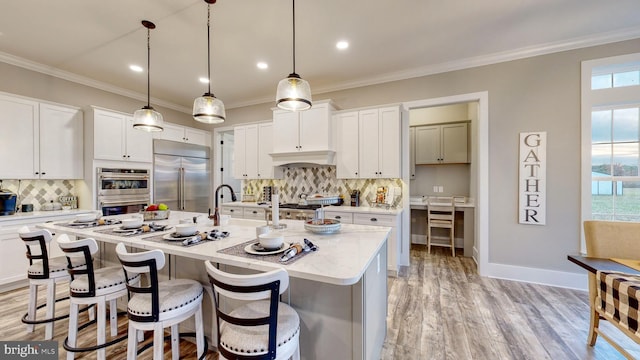 kitchen with a center island with sink, light hardwood / wood-style flooring, backsplash, appliances with stainless steel finishes, and white cabinets