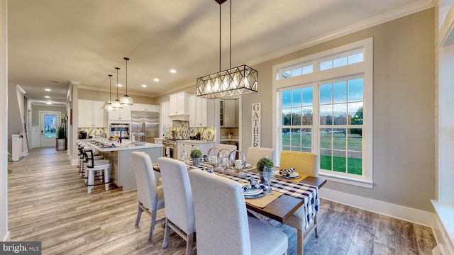 dining space featuring light wood-style floors, recessed lighting, ornamental molding, and baseboards