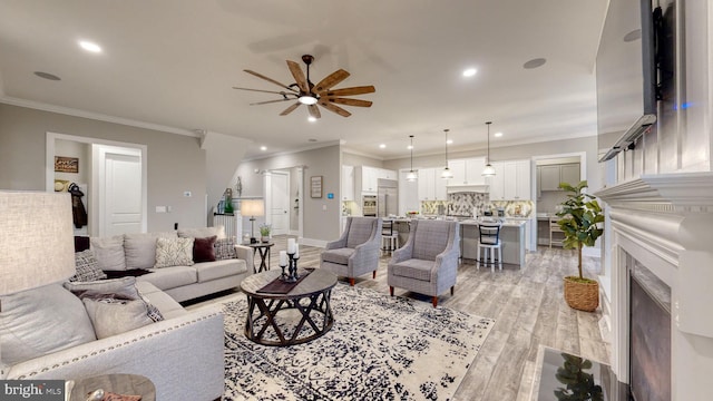 living room featuring ceiling fan, ornamental molding, a high end fireplace, and light hardwood / wood-style flooring