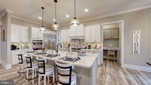 kitchen with white cabinets, backsplash, stainless steel appliances, an island with sink, and pendant lighting