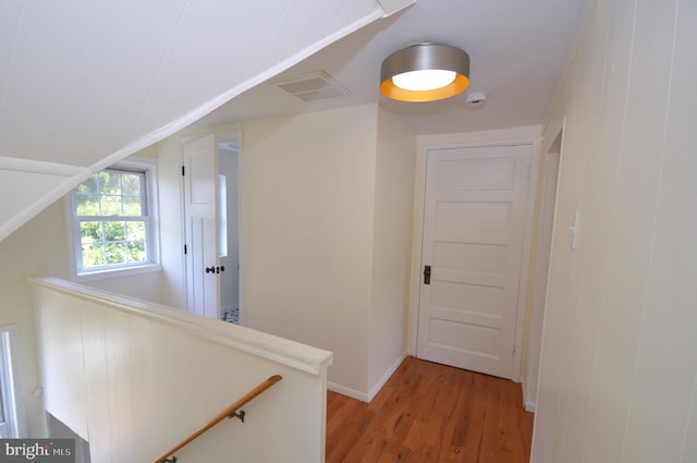 hall with light wood finished floors, visible vents, vaulted ceiling, an upstairs landing, and baseboards