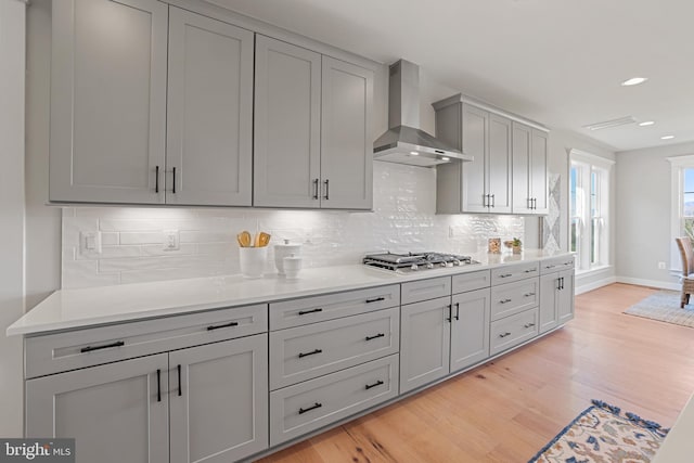 kitchen featuring stainless steel gas cooktop, gray cabinets, light countertops, light wood-style flooring, and wall chimney range hood